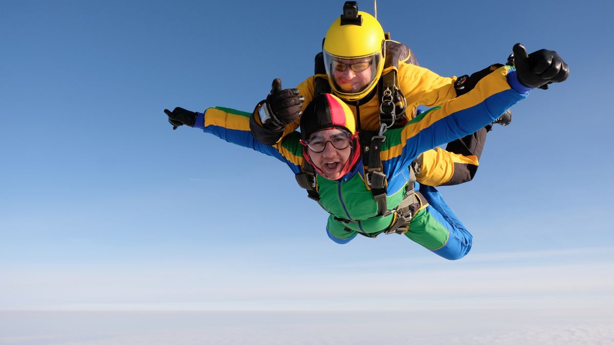 Dva skáčiaci parašutisti vo vzduchu, jeden s úsmevom a druhý s helmou.