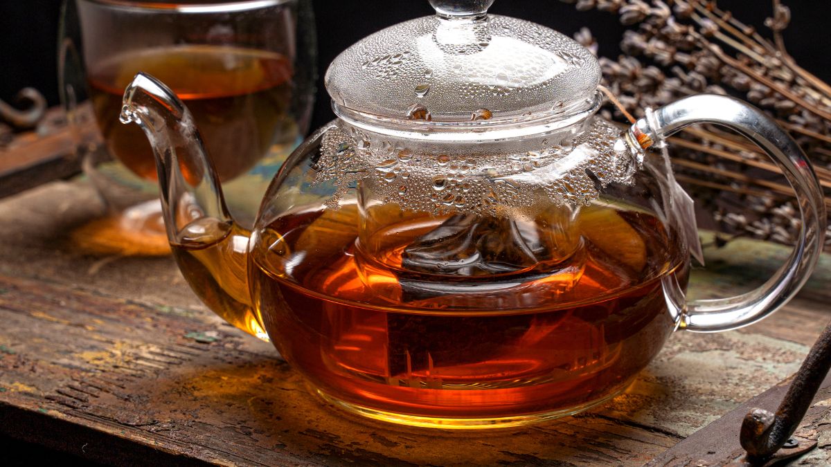 Sklenený čajník s bylinným čajom, ktorý sa varí, na drevenom stole.