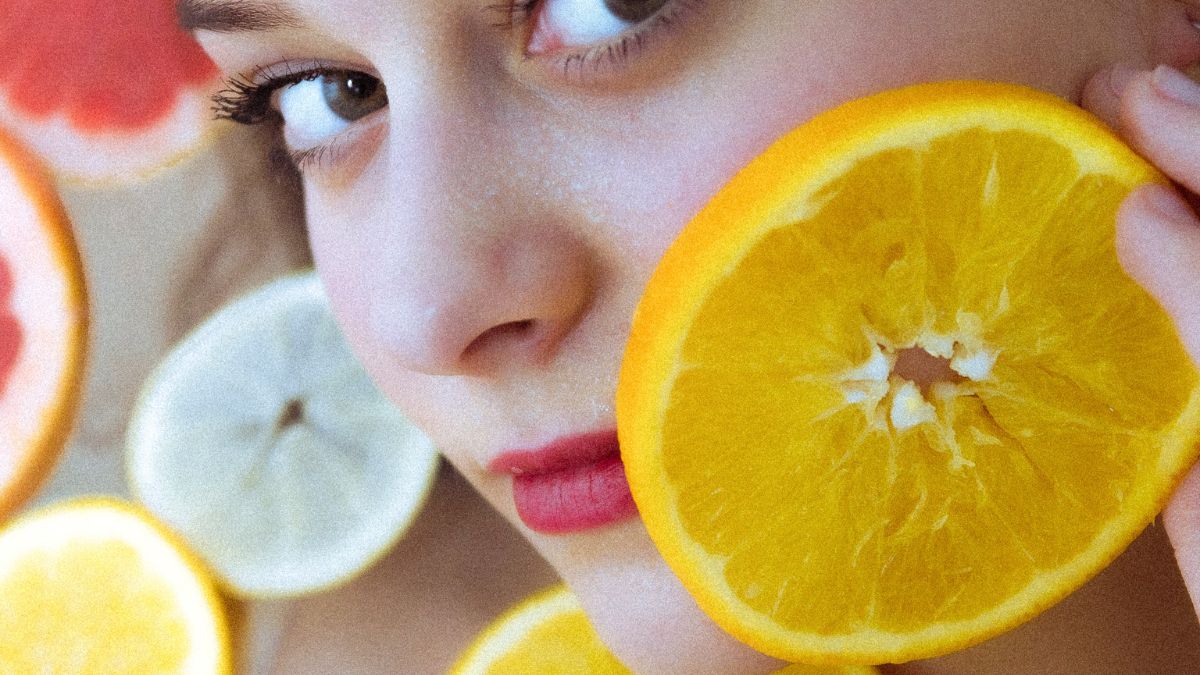 Žena s citrónom na tvári, okolo sú rôzne citrusové plody.
