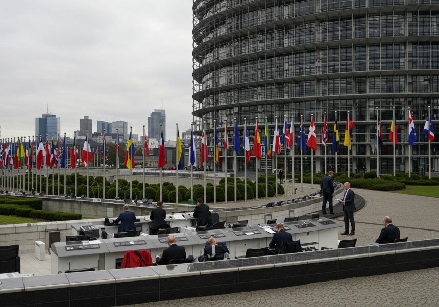 Budova Európskeho parlamentu s vlajkami členských štátov EÚ a ľuďmi na schôdzi.