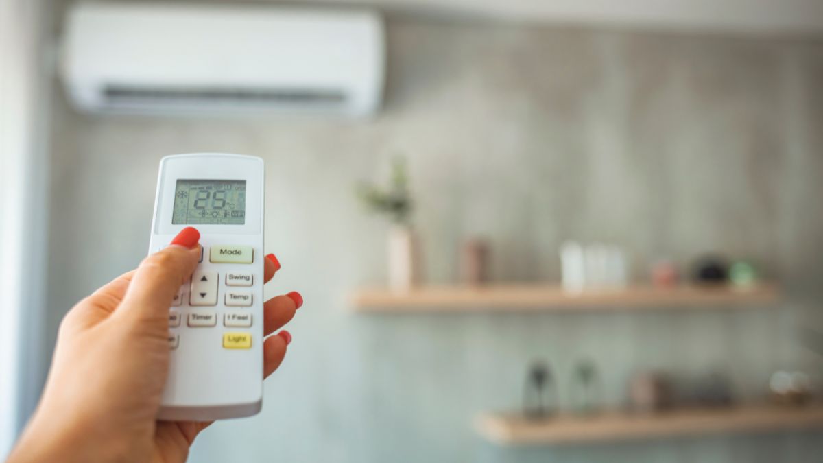 Ruka s diaľkovým ovládaním klimatizácie nastavuje teplotu na 25 °C.