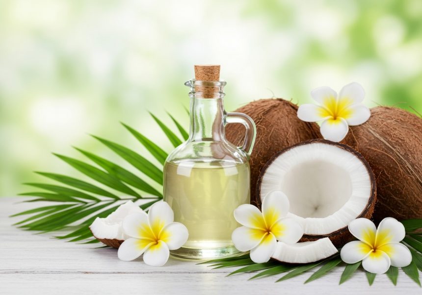 Fľaša kokosového oleja s kokosmi a kvetmi na drevenom stole.