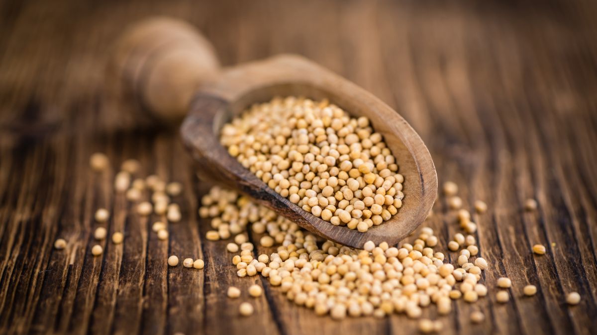 Horčičné semienka v drevenej lyžici, roztrúsené na drevenom stole.