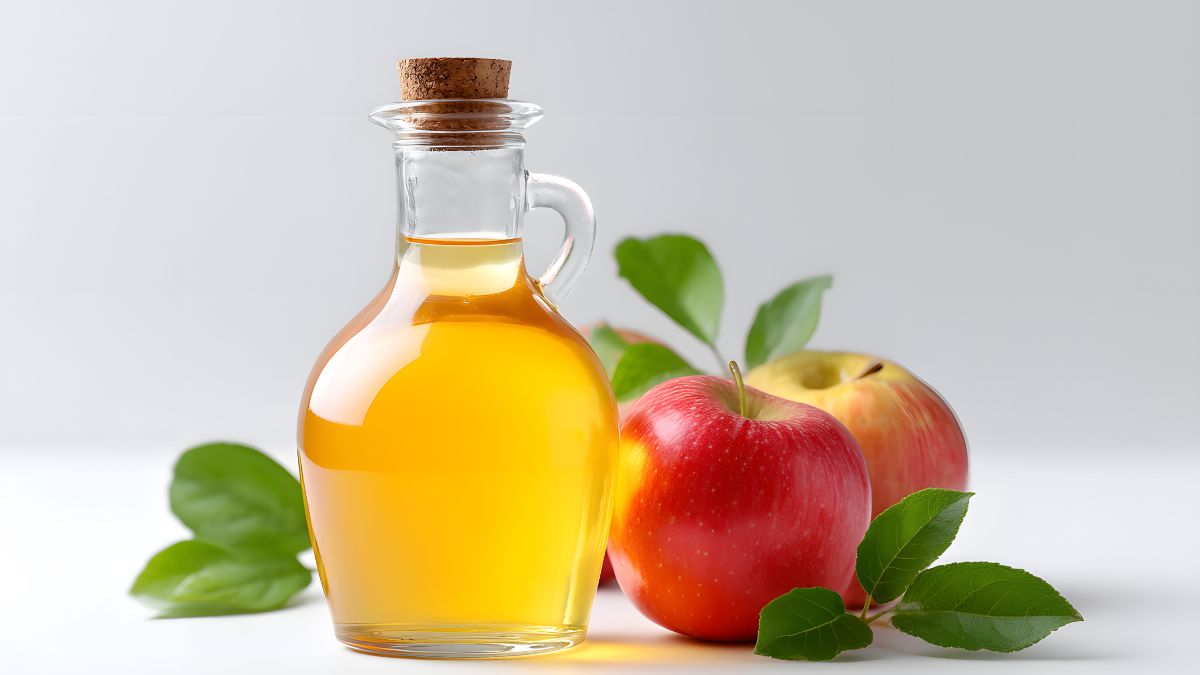 Fľaša medového jablčného octu vedľa červeného a žltého jablka.