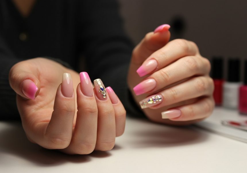 Ružové a nude umelé nechty s ozdobami na rukách ženy.