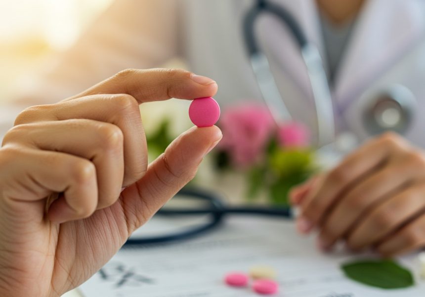 Ružová tabletka, symbol ženskej Viagry, držená v ruke, s lekárskym pozadím.