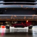 Pohľad na opotrebovaný stabilizátor pod autom s koróziou a známkami používania.