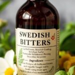 Fľaša švédskych kvapiek s bylinkami na pozadí.